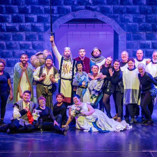 Spamalot company posing for a group photo in front of a castle backdrop