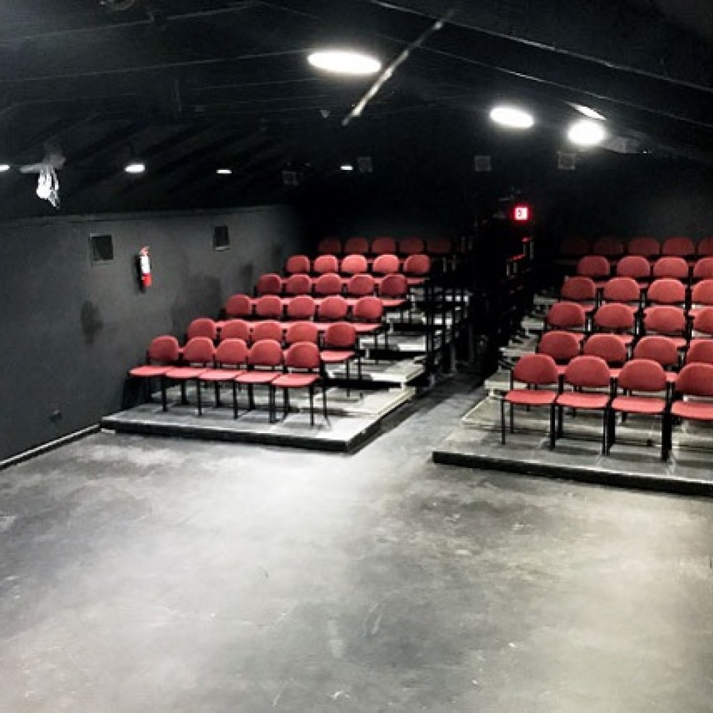 Black box theatre with several rows of red chairs on risers with a row down the middle