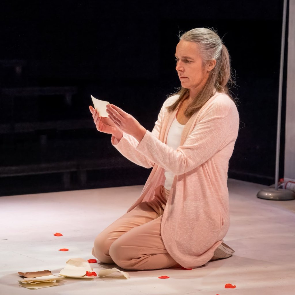 Animals Out of Paper archive photo. A woman kneels amongst torn notebook pages and rose petals. She reads one of the pages.