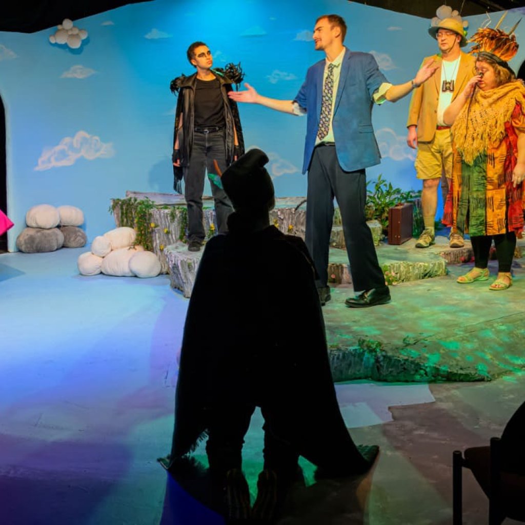 A man with his arms outstretched talks to a group of people dressed as birds