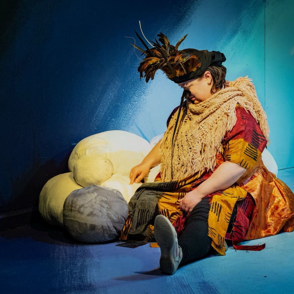 A woman dressed as a bird sits next to a stack of cloud pillows