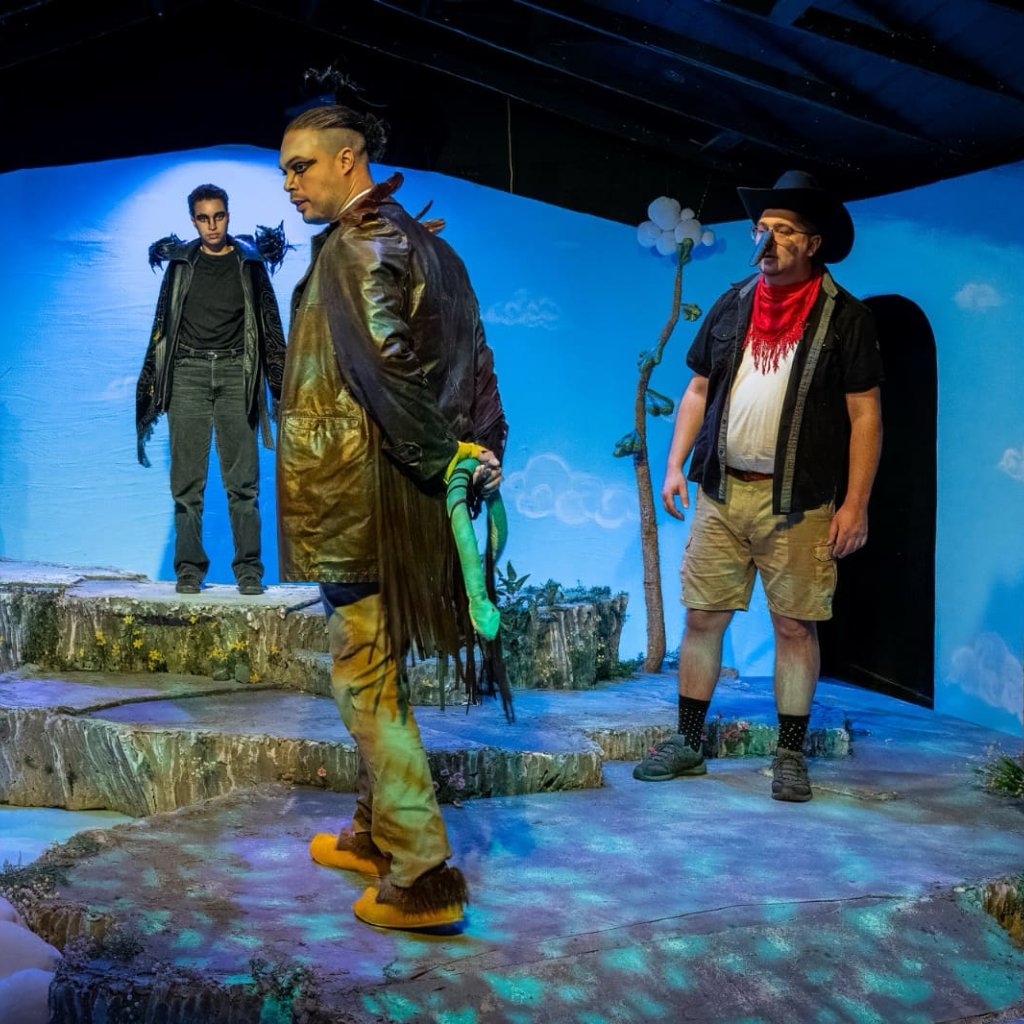 A man in a leather jacket with feathers surveys the room while three people dressed as birds look on.