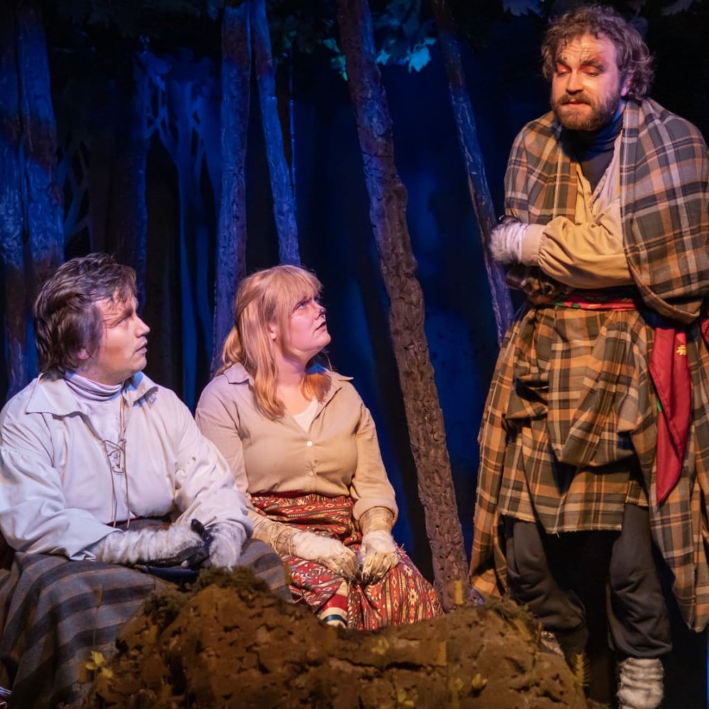Two seated characters look up at one who appears to be shivering.