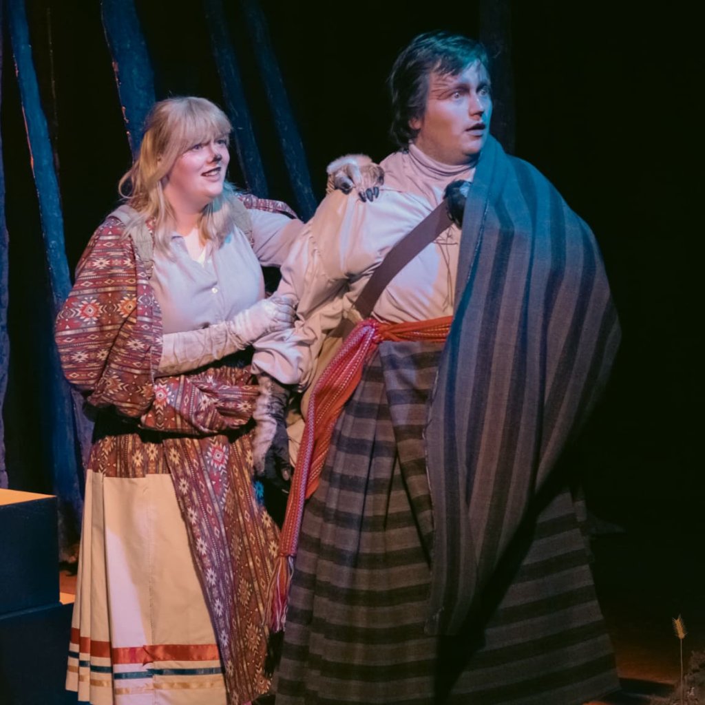 Two people looking off to the right. One standing behind the other with a hand on their shoulder.