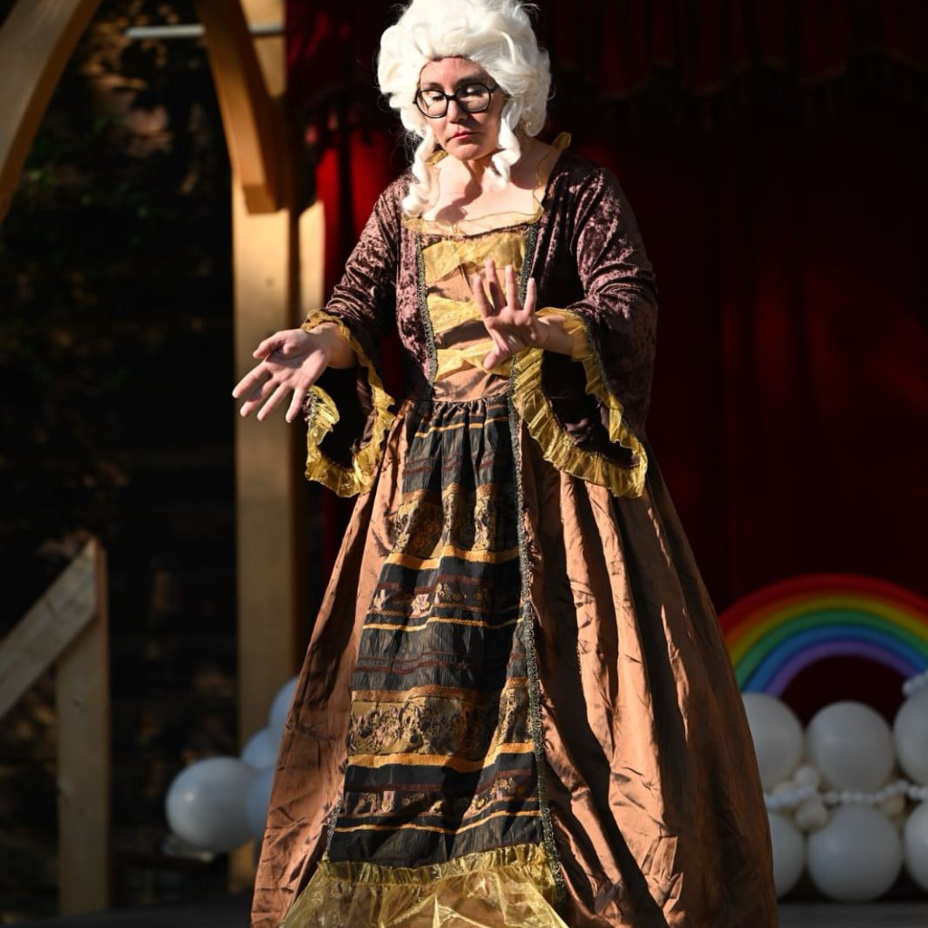 Archive photo of a Round Back performance. A woman in a large white wig and Victorian gown.